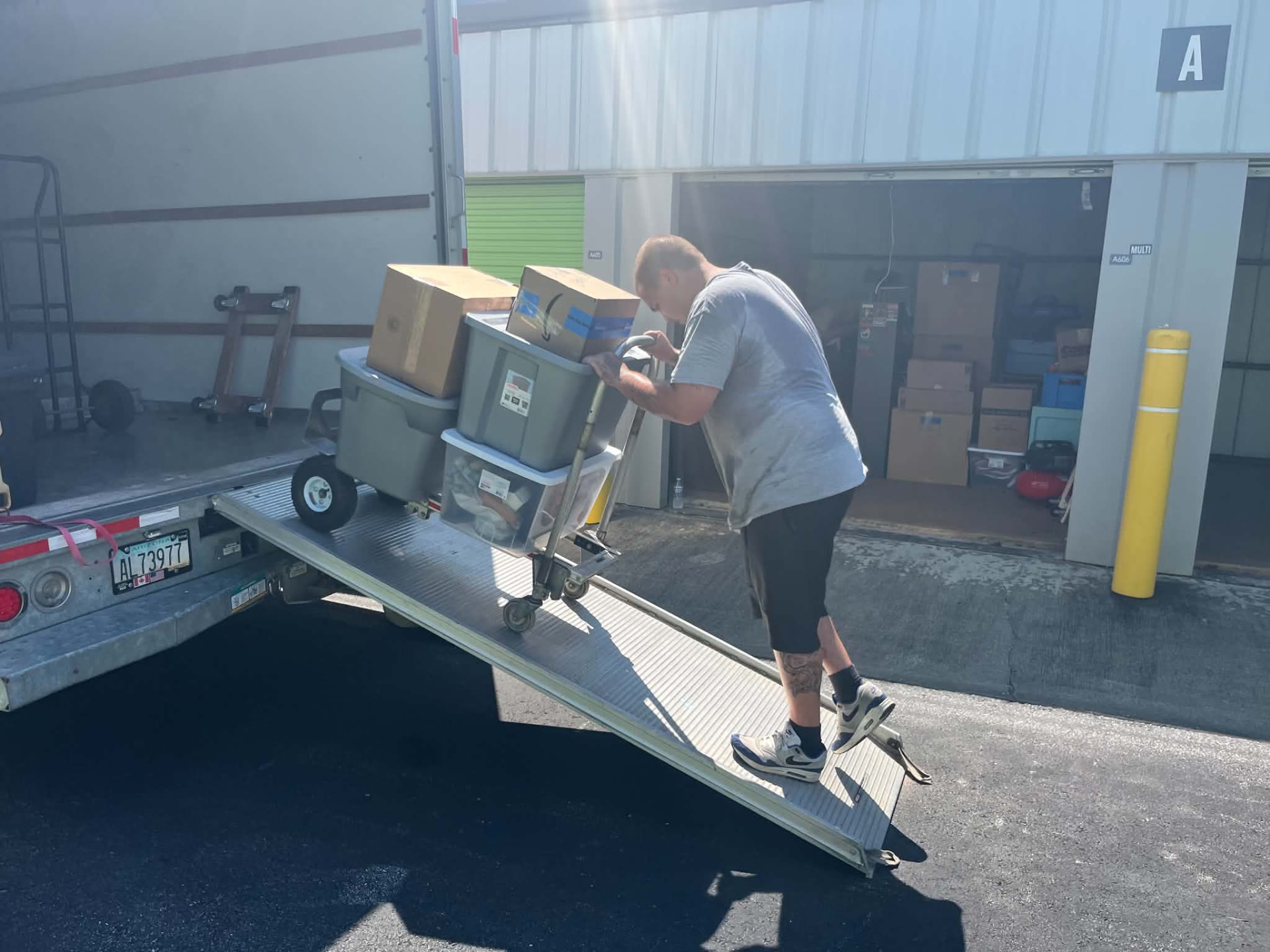 Mover rolling a dolly of boxes and bins up the truck ramp at a storage facility