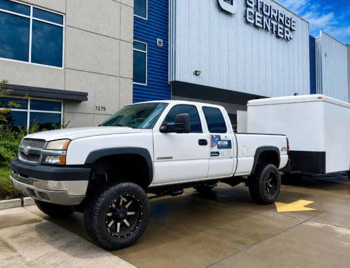 White professional moving truck with enclosed trailer at a Gulf Coast storage center
